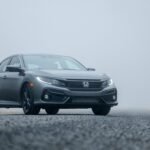 A sleek silver car parked on a foggy road, showcasing its elegance.